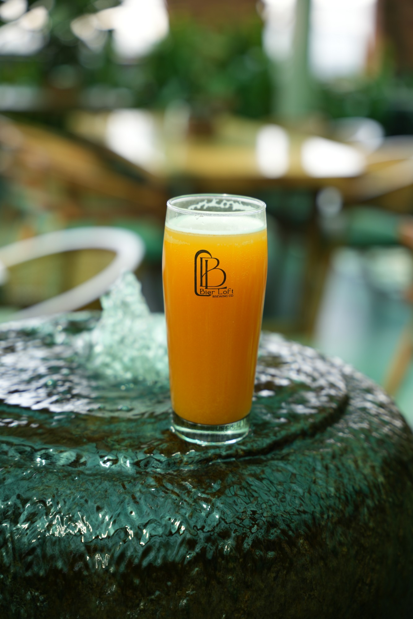 Glass of hazy craft beer resting on the stone water feature at Bier Loft