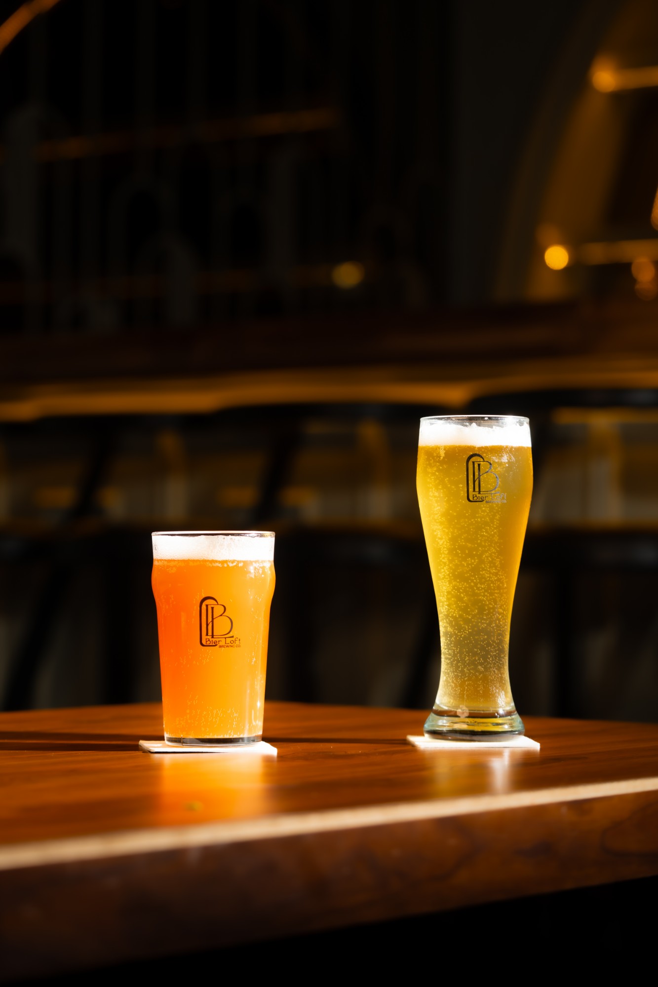 Two Bier Loft craft beers, an amber ale and a wheat beer, on a wooden bar